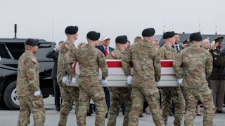 Army troops carry the American flag-covered coffin of a soldier killed in the strike on an operations center in Kuwait. Donald Trump stands in the background and salutes
