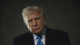 A close-up of Donald Trump's head, tilting to the left, lit from the side.