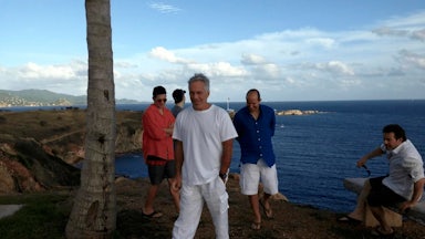 Howard Lutnick and Jeffrey Epstein smile in a group with three other men on Epstein's island, by the water.