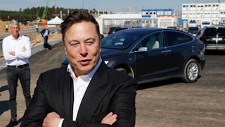 Elon Musk crosses his arms over his chest as he stands in front of a Tesla