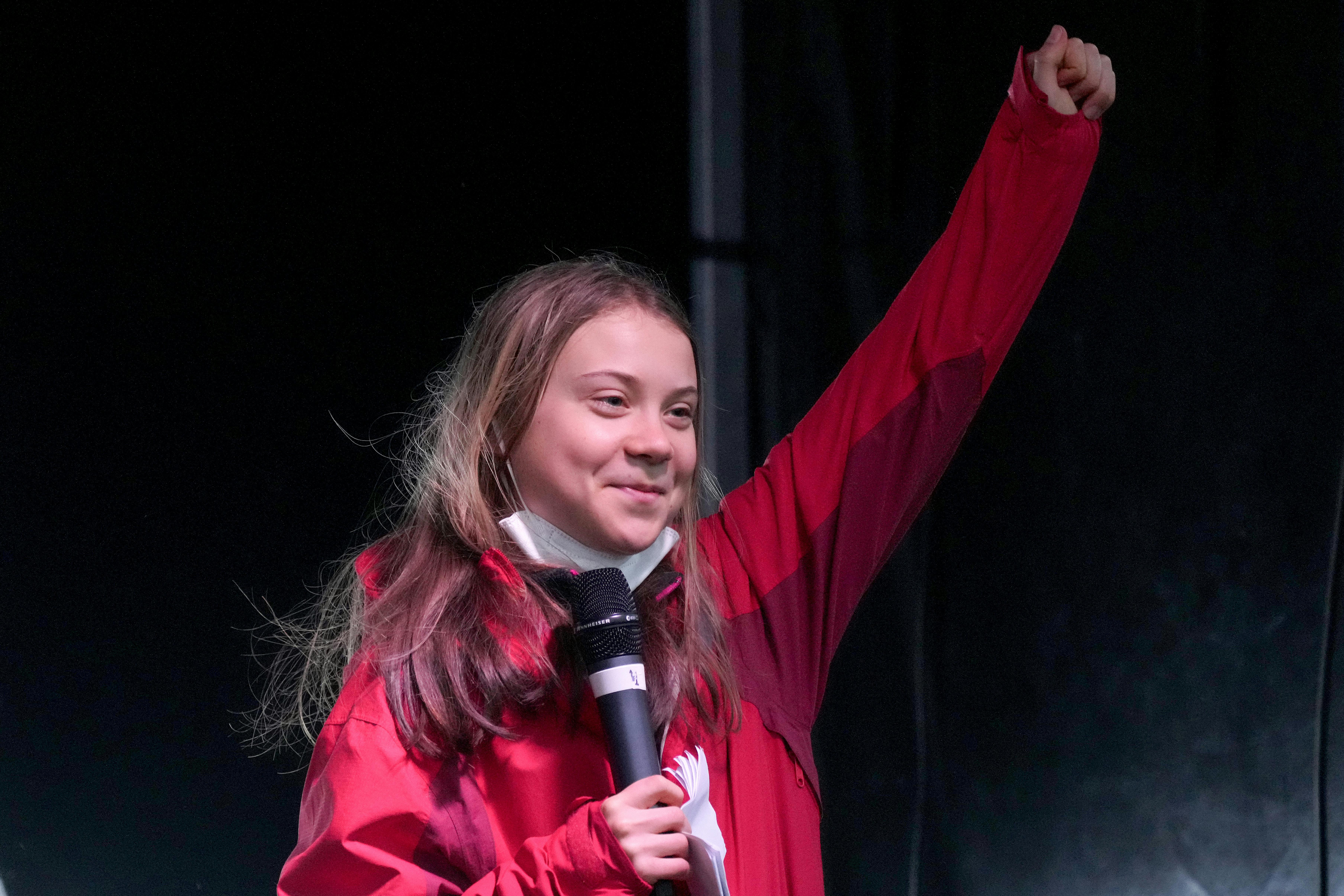 Greta Thunberg raises her fist, smiling.
