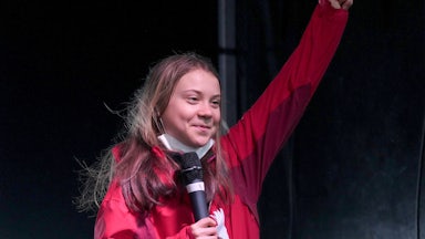 Greta Thunberg raises her fist, smiling.