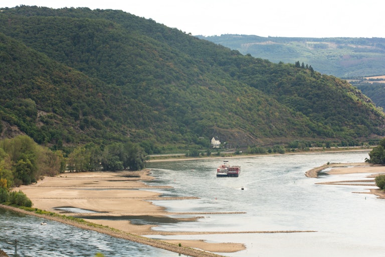Cargo ships travel on a river with wide, dry banks.