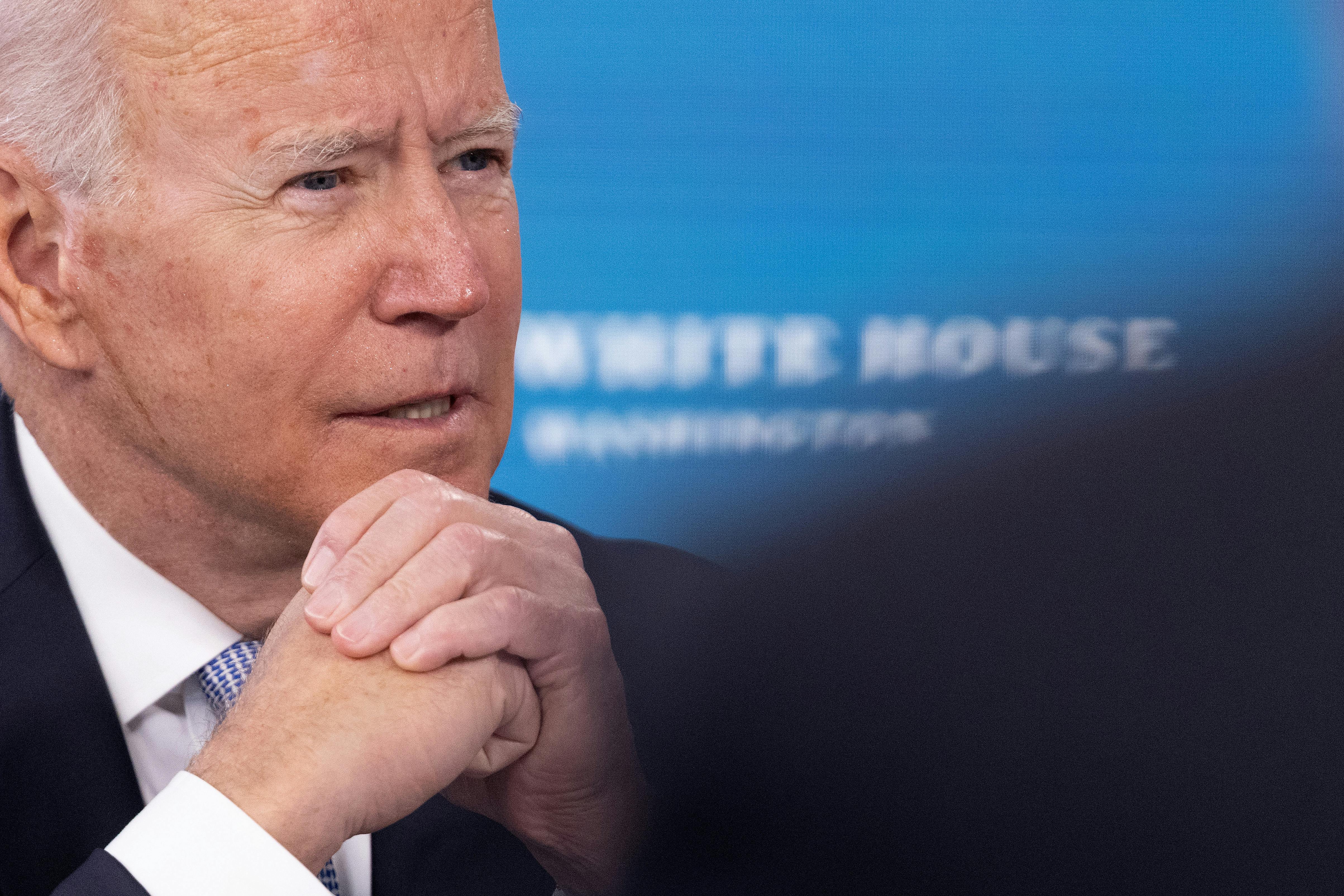 A close up of President Joe Biden, speaking with hands folded under his chin.