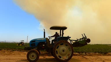 Farmers drive their tractors near a field.