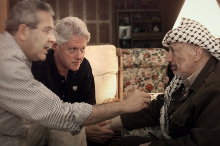 President Bill Clinton and Gamal Hamal speak closely with Yasser Arafat, touching his arm.