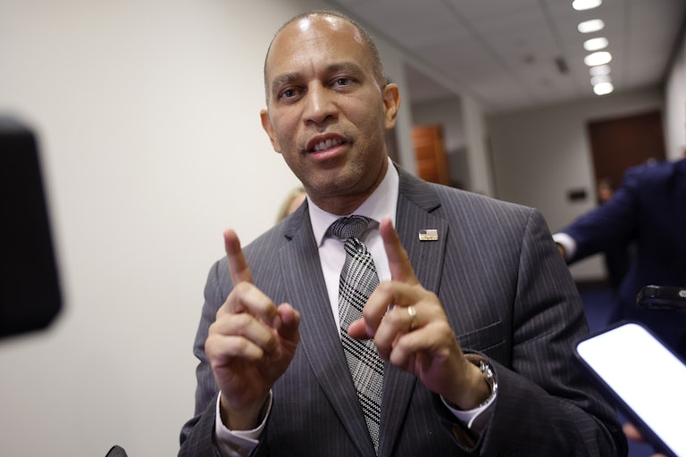 Hakeem Jeffries speaks and points both index fingers up. A gaggle of reporters surround him.