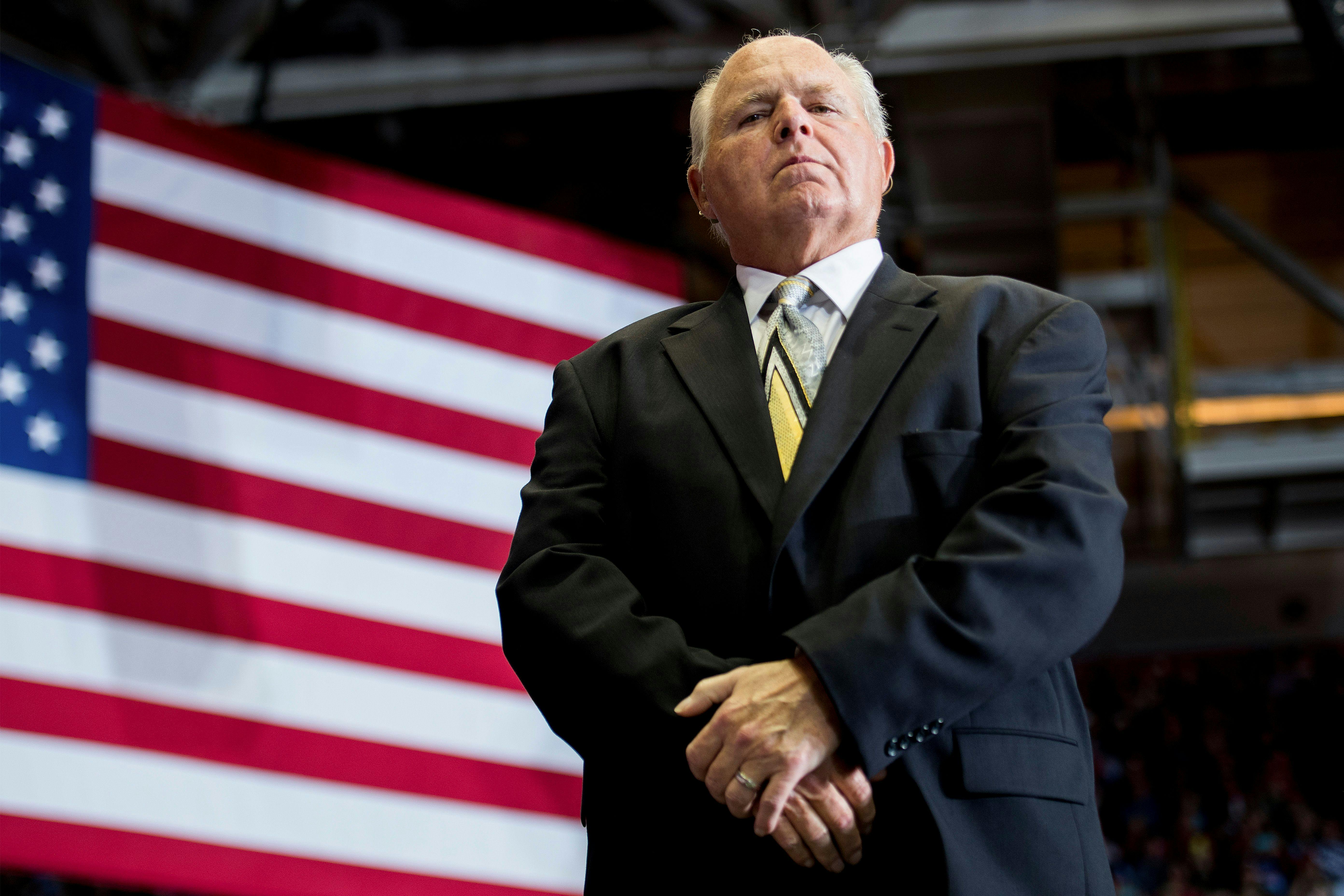 Rush Limbaugh, seen from below, standing in front of an American flag.