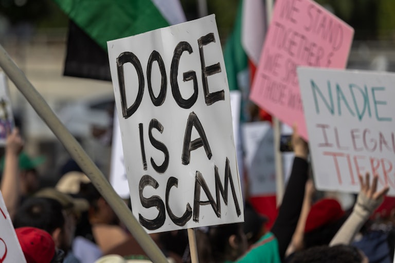 A person holds up a sign that says “DOGE is a scam” at a protest in Los Angeles, California