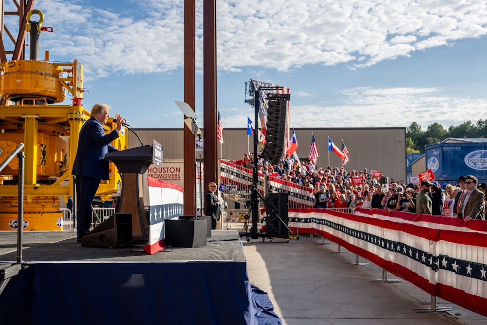 Trump stands in profile at a podium, speaking to a crowd of people.