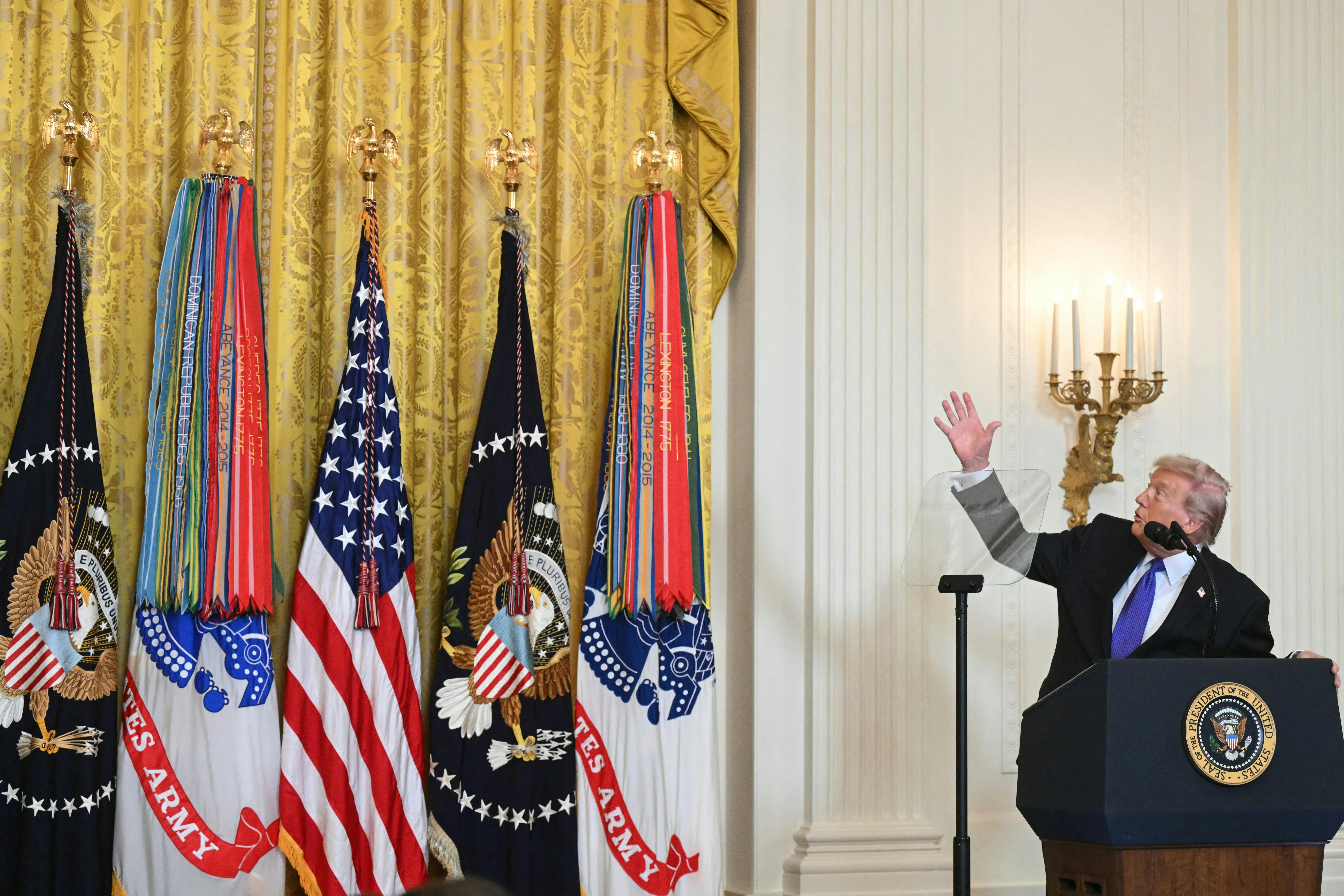 Donald Trump looks up and points at the drapes next to him, while standing at the presidential podium in the White House.