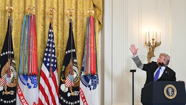 Donald Trump looks up and points at the drapes next to him, while standing at the presidential podium in the White House.