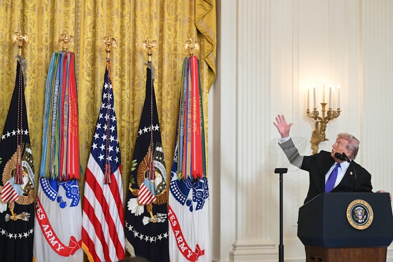 Donald Trump looks up and points at the drapes next to him, while standing at the presidential podium in the White House.