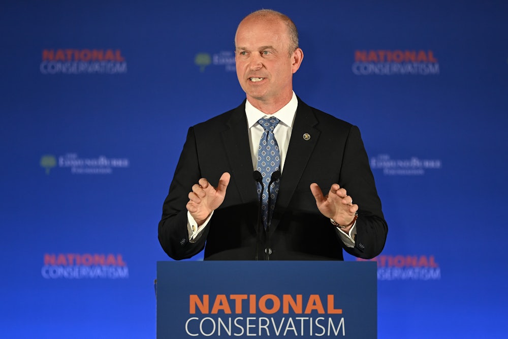 Kevin Roberts gesticulates while standing at a podium bearing the words "National Conservatism."