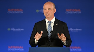 Kevin Roberts gesticulates while standing at a podium bearing the words "National Conservatism."