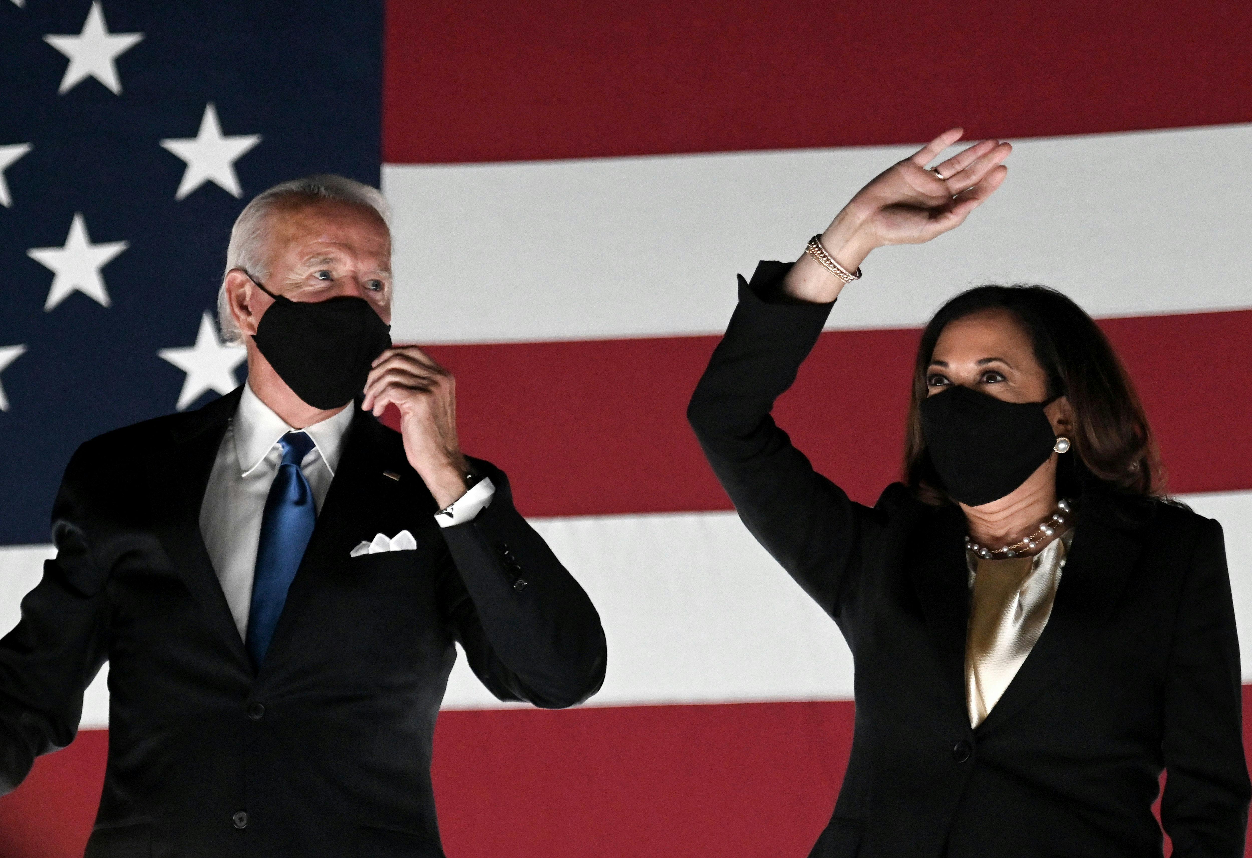 Joe Biden and Kamala Harris stand in front of an American flag backdrop