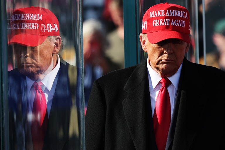 Donald Trump wearing a MAGA hat looks downward, his face partially in shadow from the sun