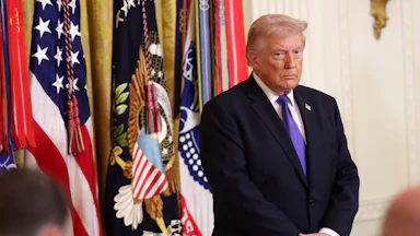 Donald Trump stands with his hands folded in front of his stomach