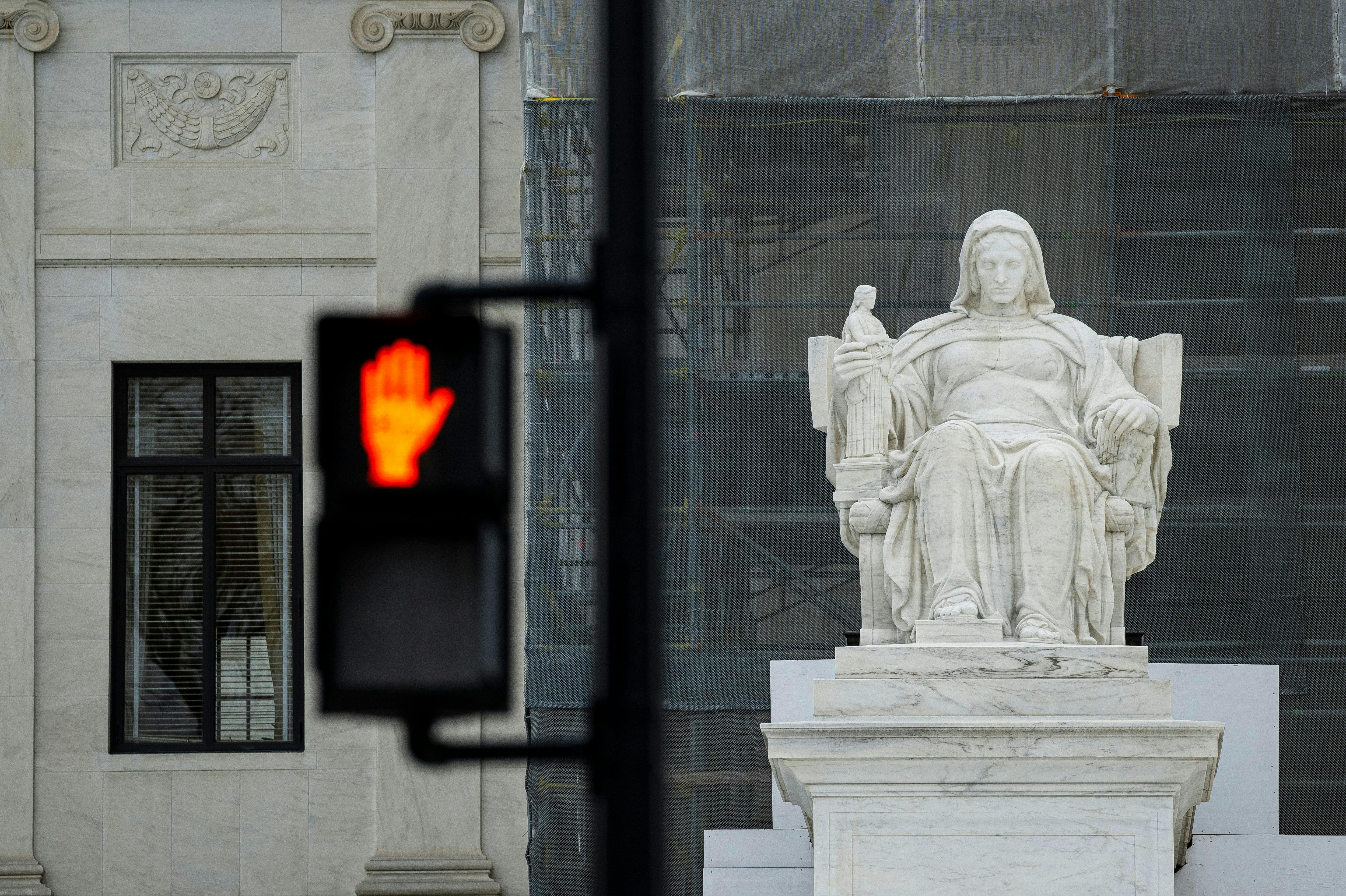 A “Don’t Walk” sign flashes in the foreground of a photograph depicting “The Contemplation of Justice” statue outside the US Supreme Court in Washington, D.C.