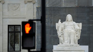 A “Don’t Walk” sign flashes in the foreground of a photograph depicting “The Contemplation of Justice” statue outside the US Supreme Court in Washington, D.C.