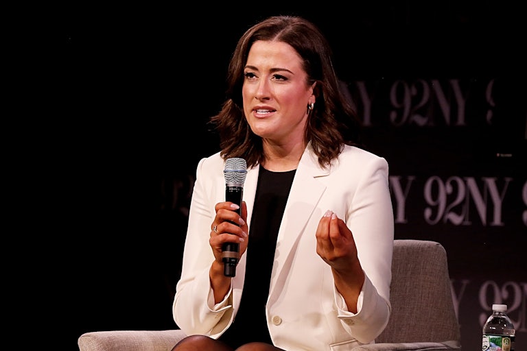 Cassidy Hutchinson wears a white blazer and is seated speaking into a mic