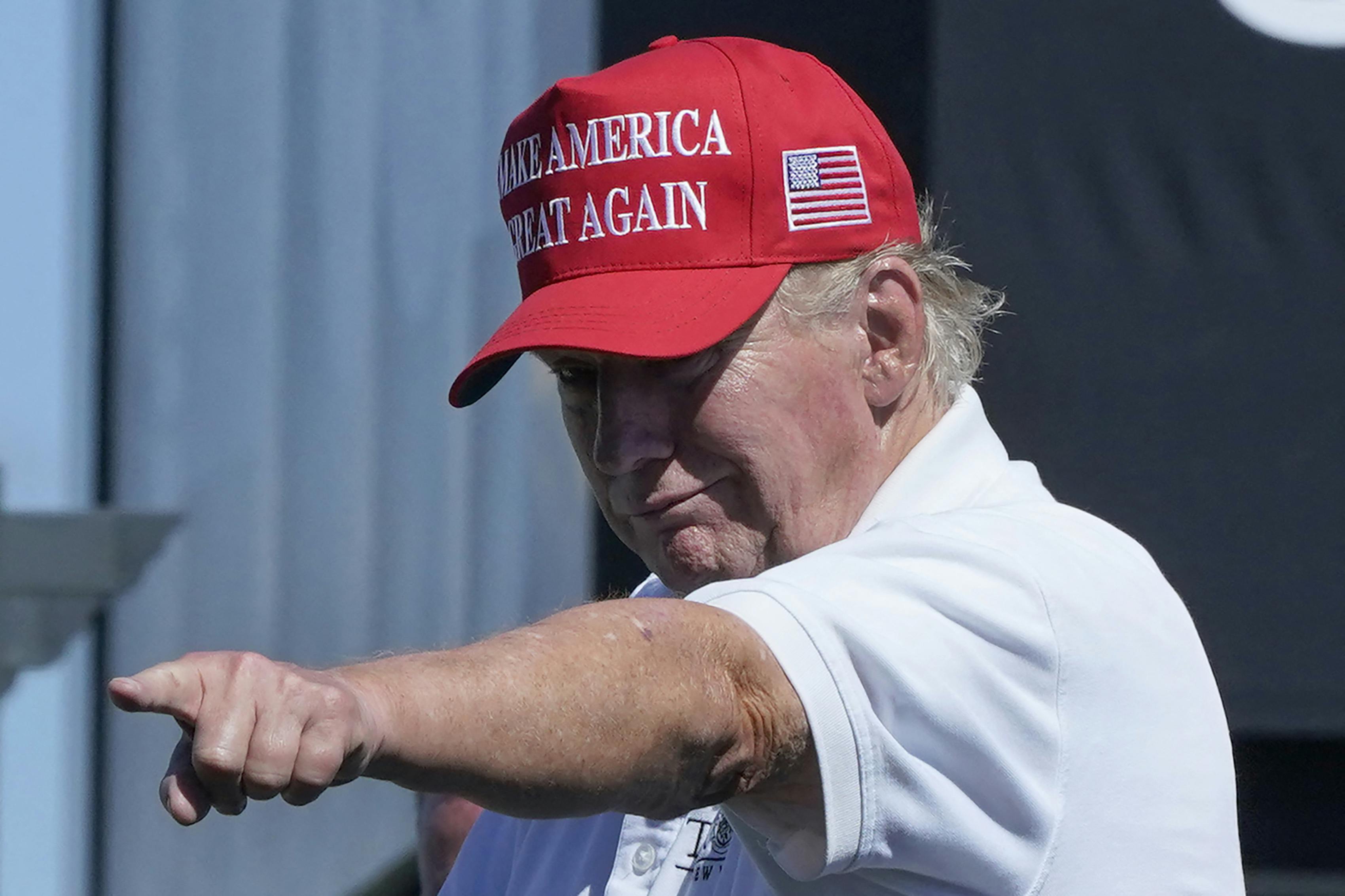 Donald Trump, wearing a red hat and a white polo shirt, points at a supporter and looks old. 