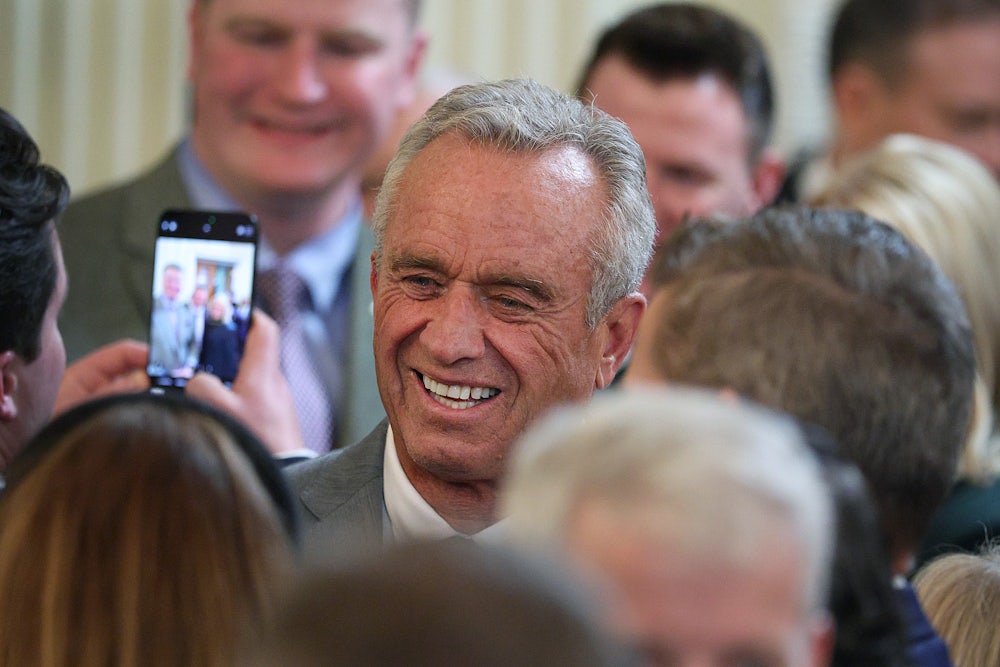 RFK Jr. smiles in a crowd as someone takes a cell phone photo of him.