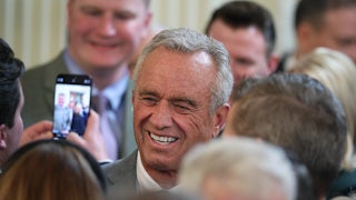 RFK Jr. smiles in a crowd as someone takes a cell phone photo of him.