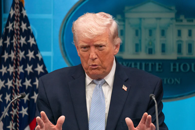 Donald Trump puckers his lips and gestures with both hands while speaking at a podium