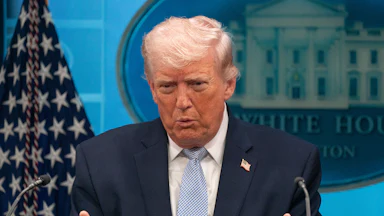 Donald Trump puckers his lips and gestures with both hands while speaking at a podium