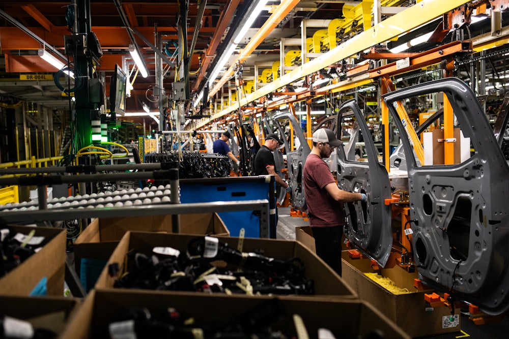 Workers adjust car doors on an assembly line.