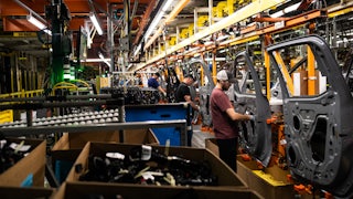 Workers adjust car doors on an assembly line.