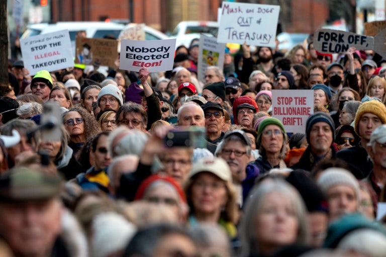 People hold up signs calling out Elon Musk during a protest outside the U.S. Treasury building in Washington, D.C.