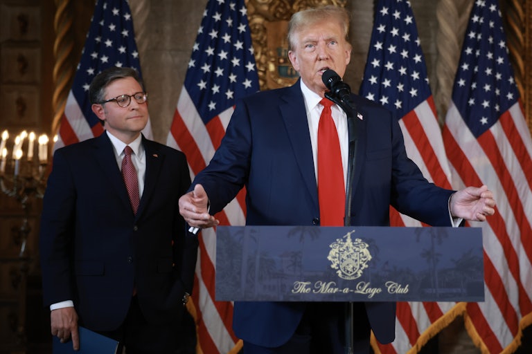 Donald Trump speak at a lectern while Mike Johnson stands behind him and looks on