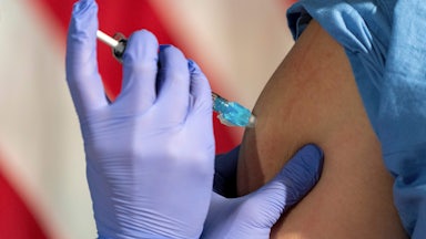 Close-up of a nurse administering a Covid vaccine in front of an American flag.