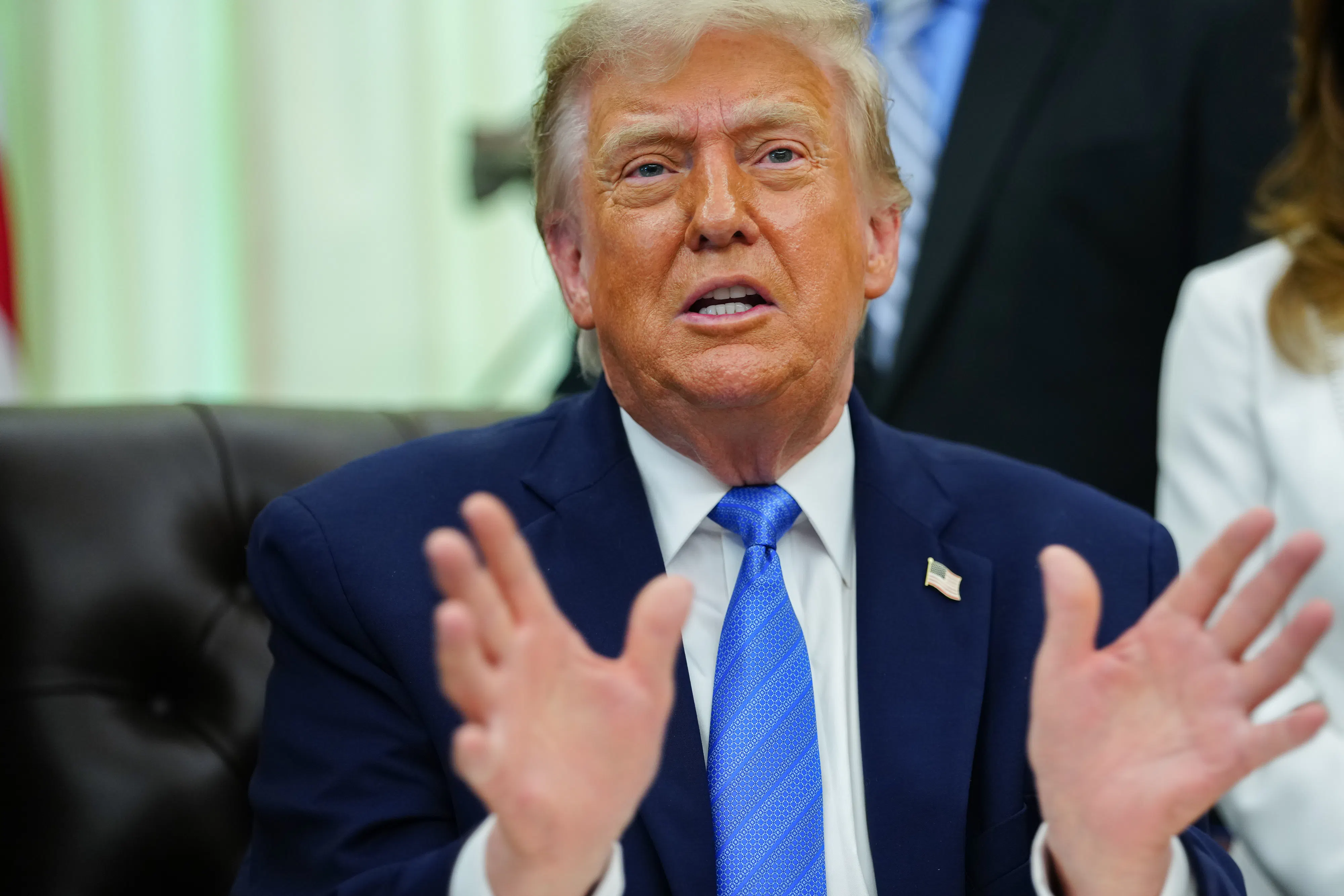 Donald Trump gestures and speaks while sitting at his desk in the Oval Office