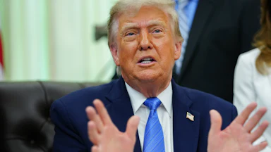 Donald Trump gestures and speaks while sitting at his desk in the Oval Office