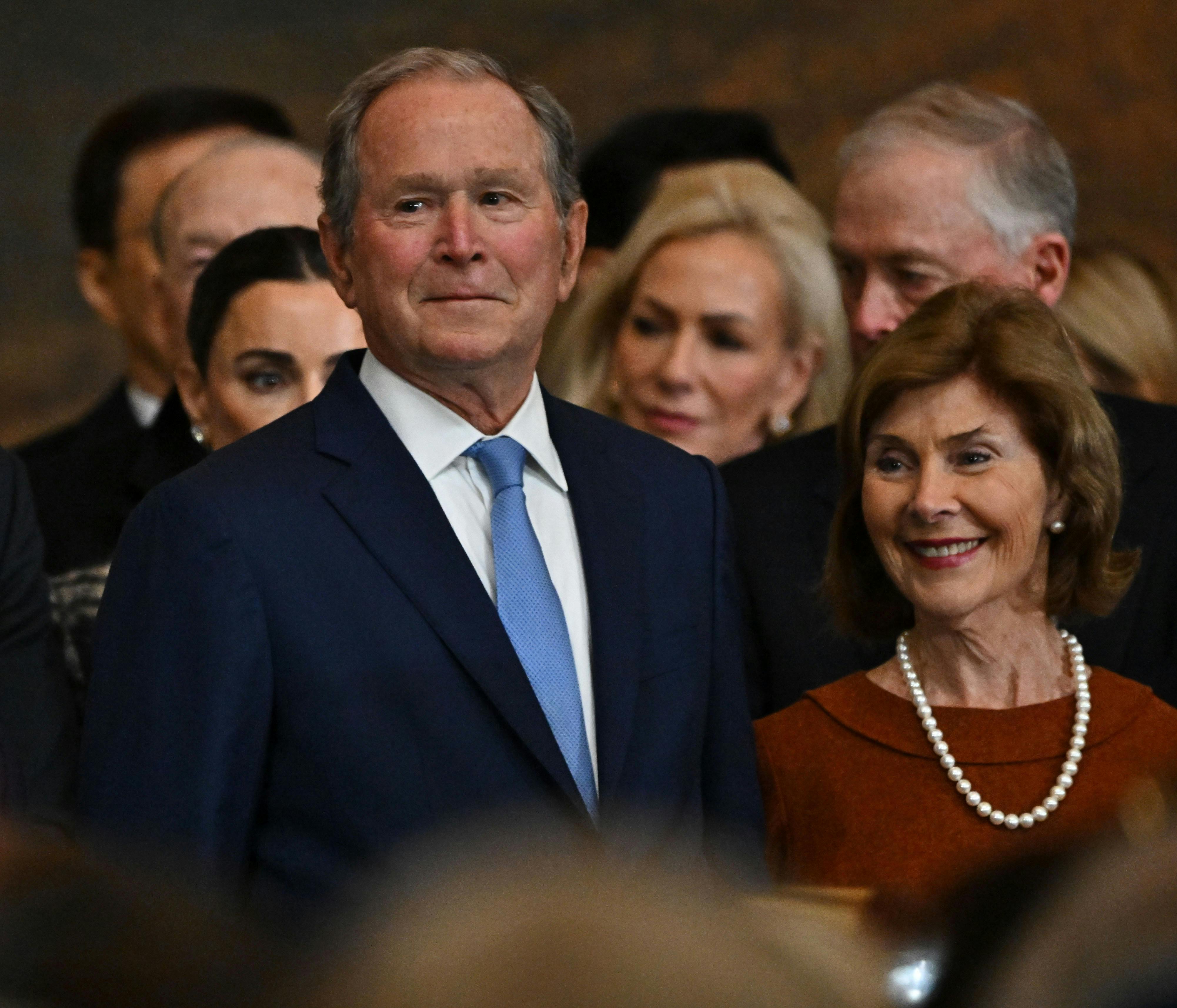 George W. Bush does his little smirk thing at Trump's inauguration. He's standing with his wife Laura, who is smiling. 