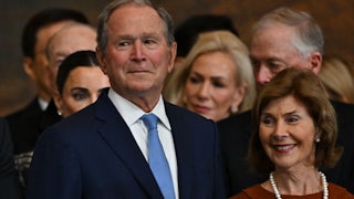 George W. Bush does his little smirk thing at Trump's inauguration. He's standing with his wife Laura, who is smiling.