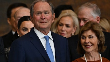 George W. Bush does his little smirk thing at Trump's inauguration. He's standing with his wife Laura, who is smiling.