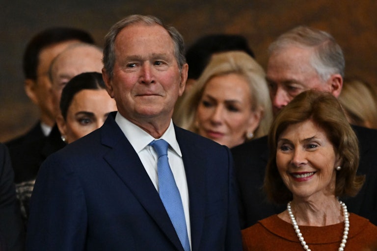 George W. Bush does his little smirk thing at Trump's inauguration. He's standing with his wife Laura, who is smiling.
