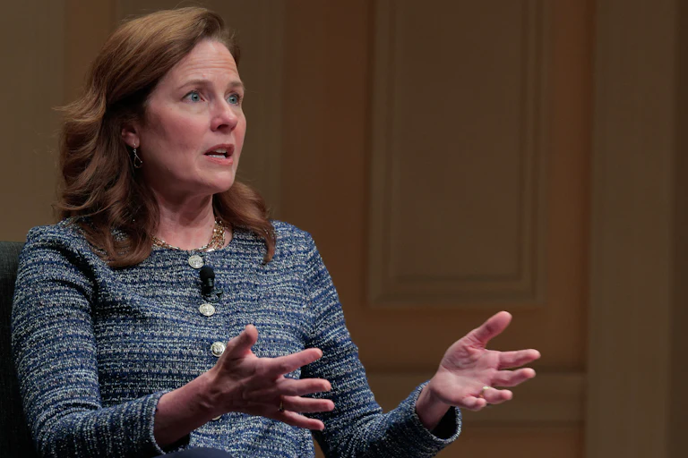 Supreme Court Justice Amy Coney Barrett speaks and gestures while sitting during an event