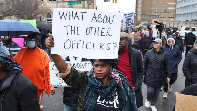 A Black protester holds a sign reading, "What about the other officers?"