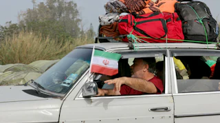 A man holds an Iranian flag as displaced residents make their way back to their homes on a makeshift road, built at the site where the Qasmieh bridge was destroyed in Israeli strikes, in the southern Lebanese area of Al-Qasmiyeh on April 18, 2026.
