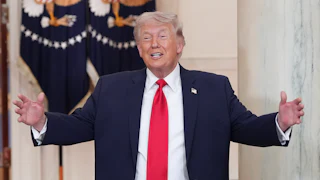 President Donald Trump smiles in the White House and spreads his arms out as if he's about to embrace or greet someone.