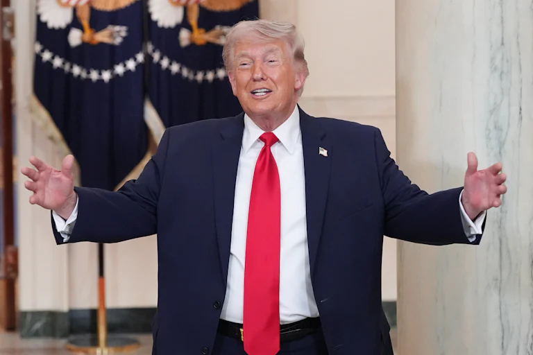 President Donald Trump smiles in the White House and spreads his arms out as if he's about to embrace or greet someone.