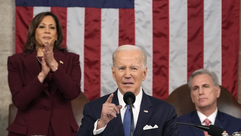 Joe Biden delivers his State of the Union. Behind him, Kamala Harris stands to clap. Kevin McCarthy remains seated and looks on.