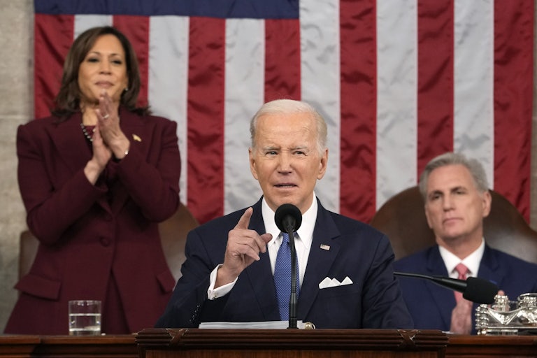 Joe Biden delivers his State of the Union. Behind him, Kamala Harris stands to clap. Kevin McCarthy remains seated and looks on.