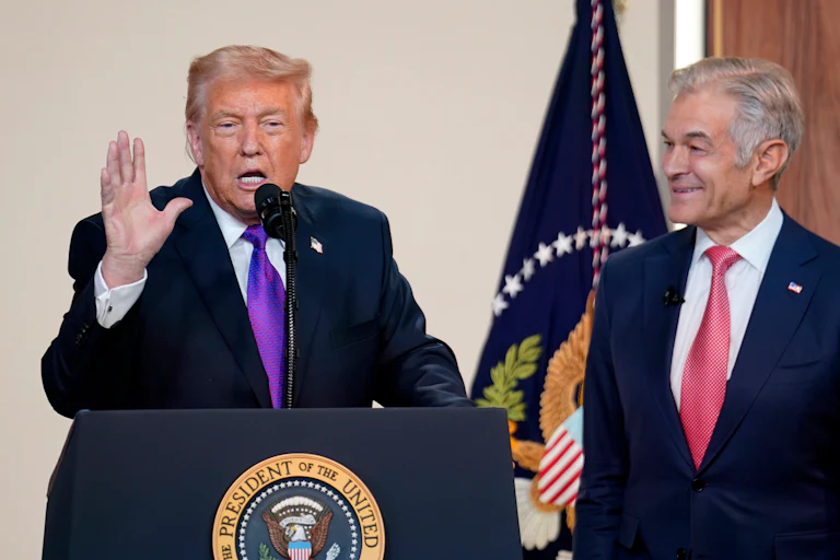 Donald Trump raises one hand while speaking at a podium. Dr. Oz stands to his left and smiles at him.