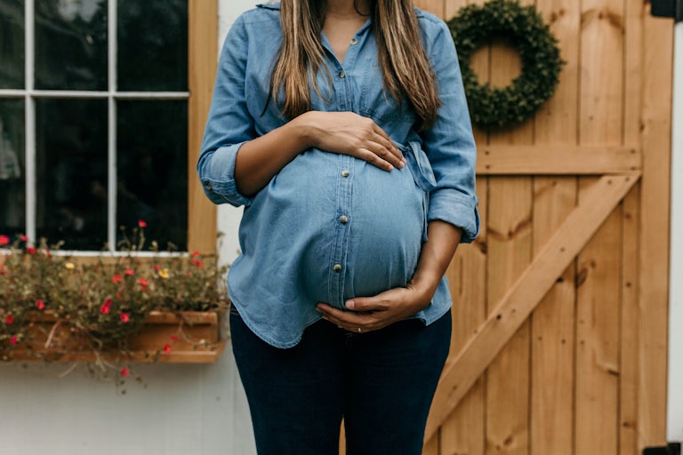 A pregnant person with their hand over their protruding belly